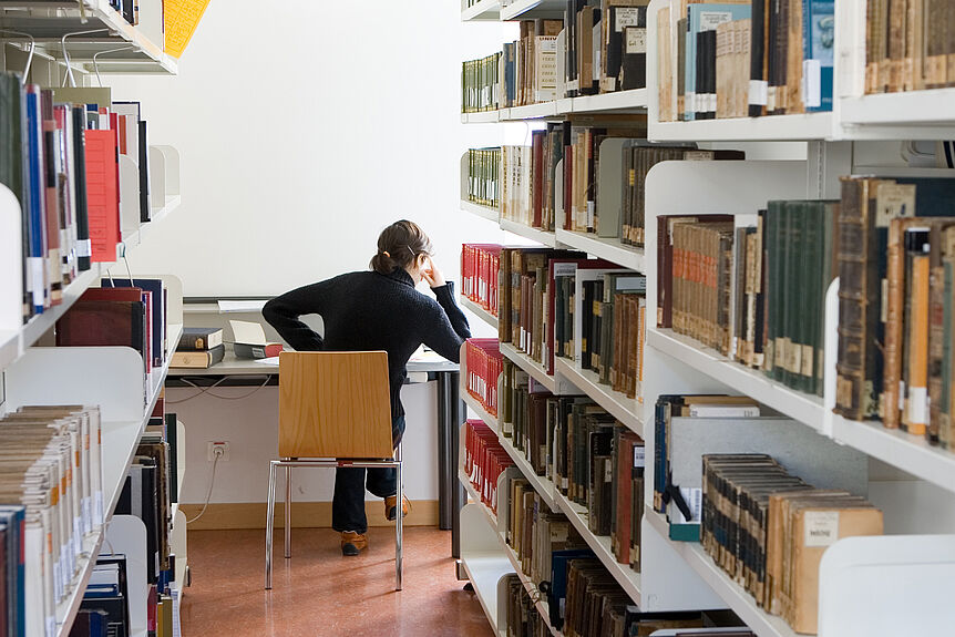 Frau sitzt in einer Fachbereichsbibliothek.