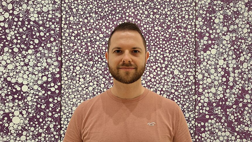 Damian Sobota, PhD (c) private; head with short brown hair and a beard. Light brown t-shirt in front of a a purple and white wallpaper