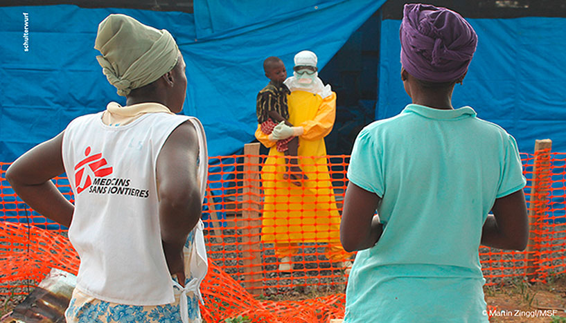 Afrikanische Frauen vor einem Mann in Schutzkleidung, der ein kleines Kind auf dem Arm hält