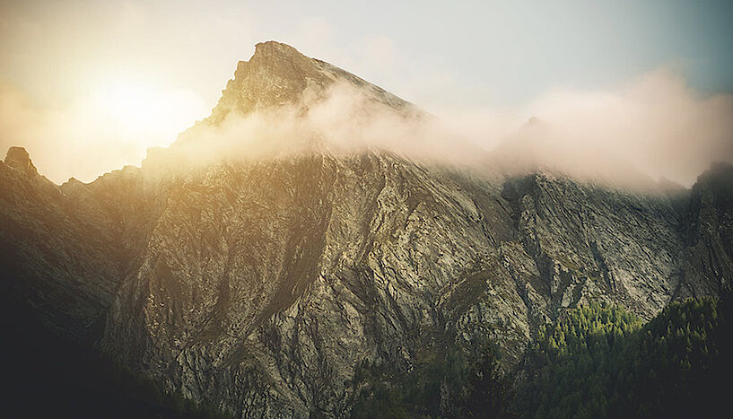 Sun rising behind a mountain peak shrouded by clouds